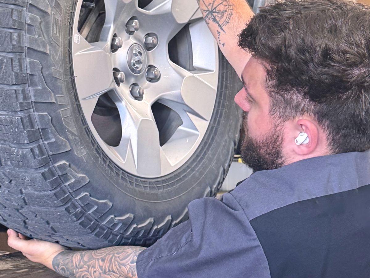 Alex holding a mounted tire and wheel beside a raised vehicle at Mad Hatter Auto Repair in Omaha, Nebraska.